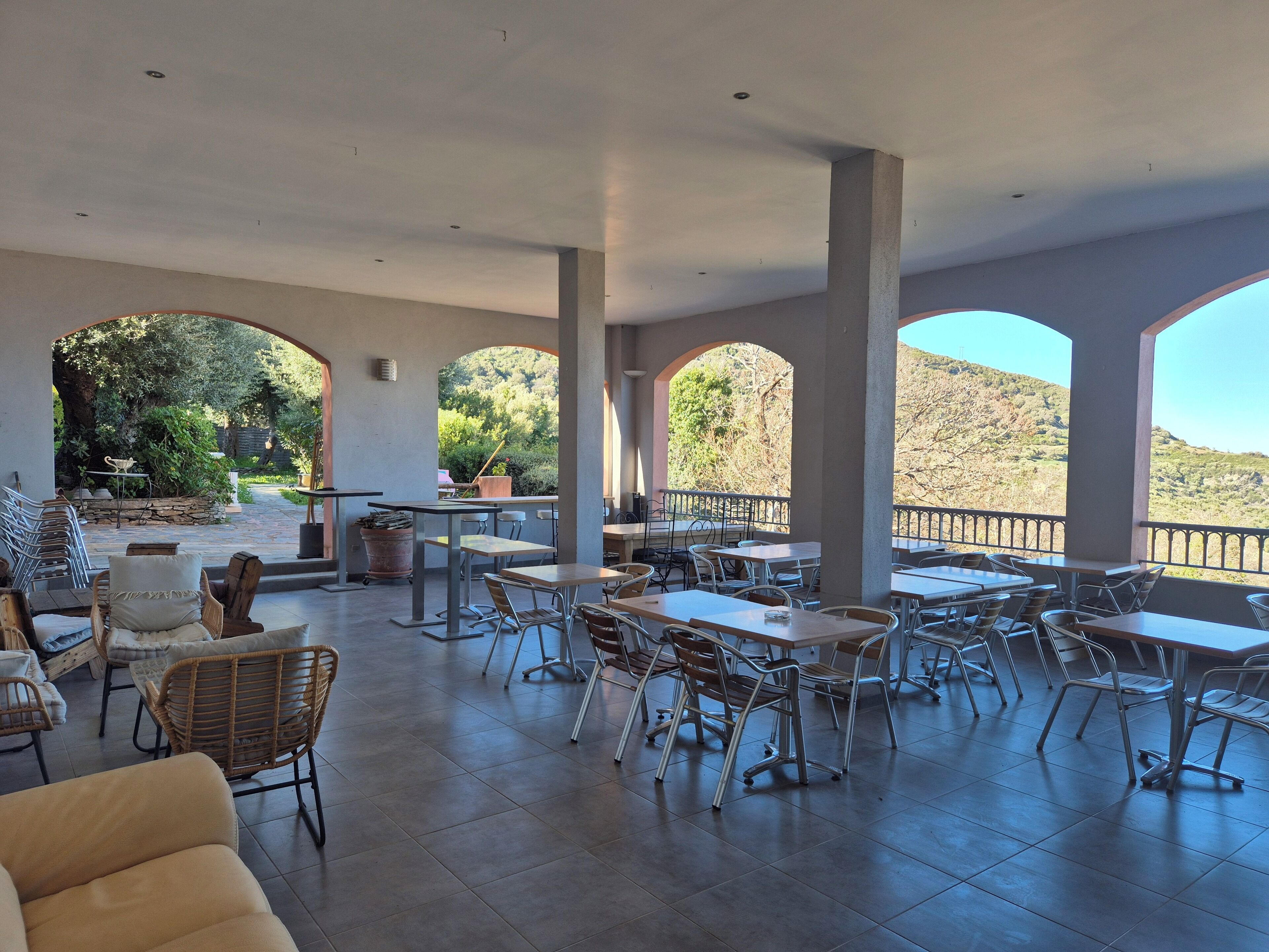 Un patio al aire libre con mesas y sillas, rodeado de arcos y vistas a un paisaje montañoso.