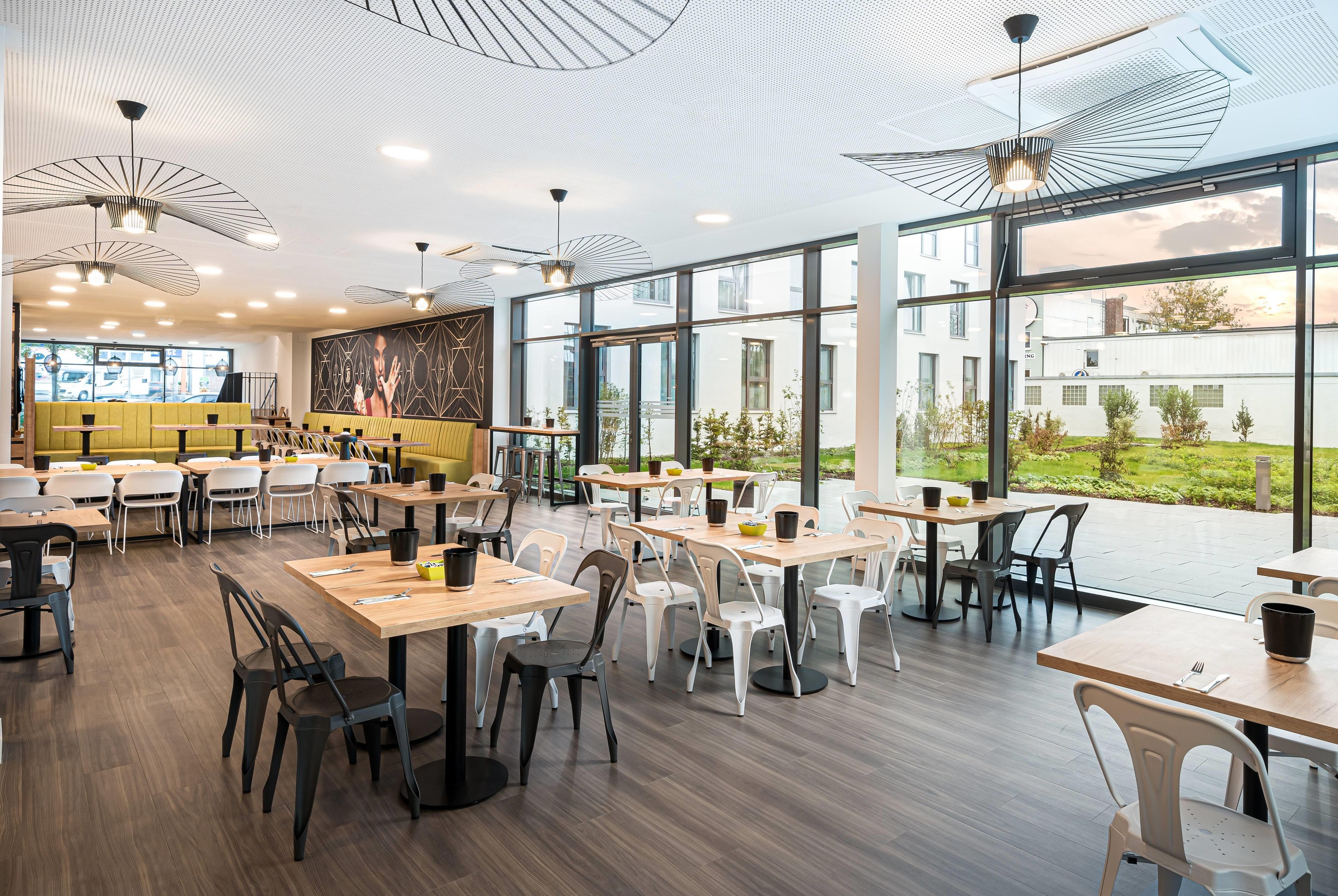 Un restaurante moderno con techos altos, amplias ventanas y diversas opciones de asientos.