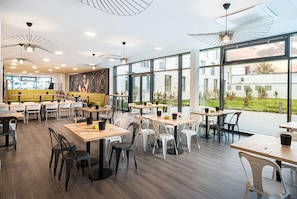 A modern restaurant with high ceilings, large windows, and a variety of seating options. - elaya hotel augsburg, Trademark by Wyndham (Augsburg)