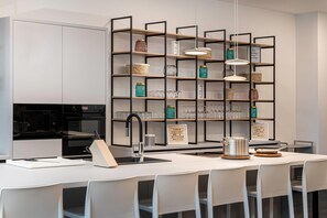 A modern kitchen with a central island, a built-in oven, and a black range hood. - elaya hotel augsburg, Trademark by Wyndham (Augsburg)