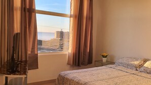 A bedroom with a bed, a desk, a lamp, and a view of the ocean. - New beautiful Ocean View Apartment (Tijuana)
