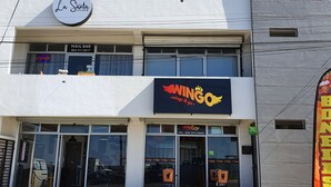 A multi-story building with a 'La Santa Nail Bar' and 'Wingo Wings & Go' restaurant on the ground floor. - New beautiful Ocean View Apartment (Tijuana)