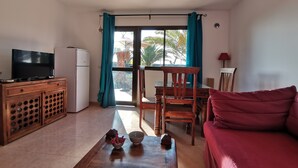 Een woonkamer met een televisie, een houten kast, een rode bank en een eethoek met een tafel en stoelen.