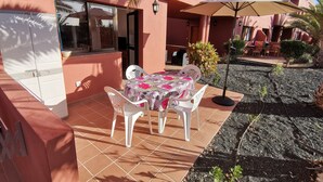 Een terras met een tafel en stoelen, een kleine tuin en een gebouw met een roze gevel.