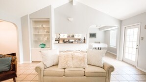 A spacious living room with a beige sofa, a coffee table, and a bookshelf.