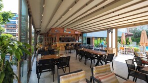 An outdoor dining area with tables and chairs, a bar, and a poolside area with umbrellas. -  CLEOPATRA ICARIA APART HOTEL (Alanya)