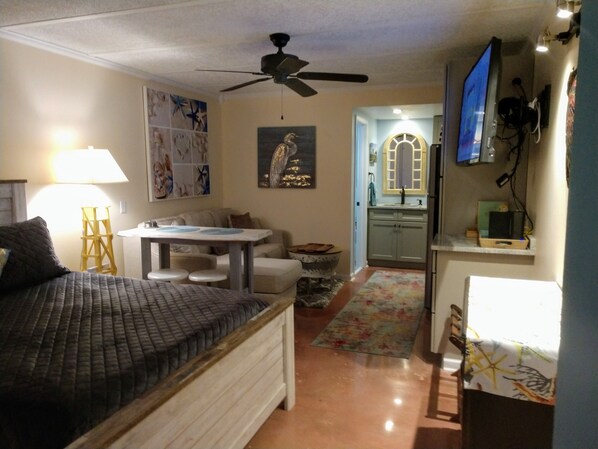 A bedroom with a bed, a ceiling fan, a small table, a sofa, and a bathroom with a sink and mirror.