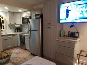A compact kitchen with a refrigerator, oven, microwave, and a television displaying a news program.