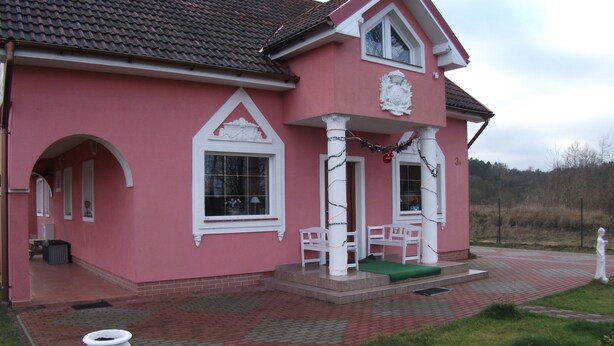 A pink house with a tiled roof, white columns, and a green door. - Pink holiday house 10 pers. between lagoon and heather in the bird sanctuary (Nowe Warpno)