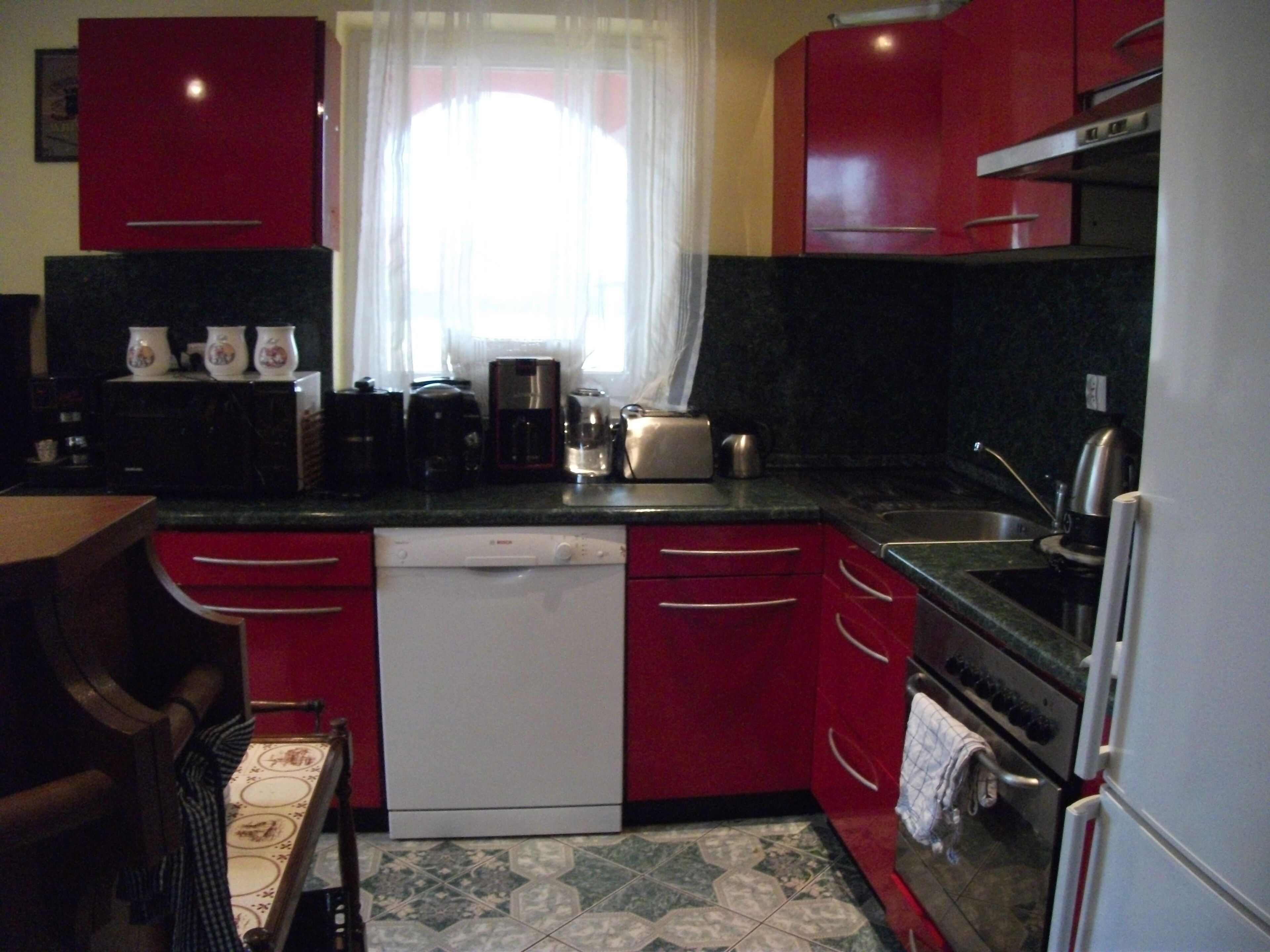 A kitchen with red cabinets, a dishwasher, a coffee maker, and a toaster.