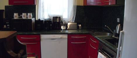 A kitchen with red cabinets, a dishwasher, a coffee maker, and a toaster.