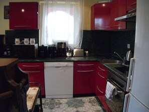 A kitchen with red cabinets, a dishwasher, a coffee maker, and a toaster.