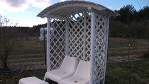A gazebo with a lattice design and two white plastic lounge chairs. - Pink holiday house 10 pers. between lagoon and heather in the bird sanctuary (Nowe Warpno)