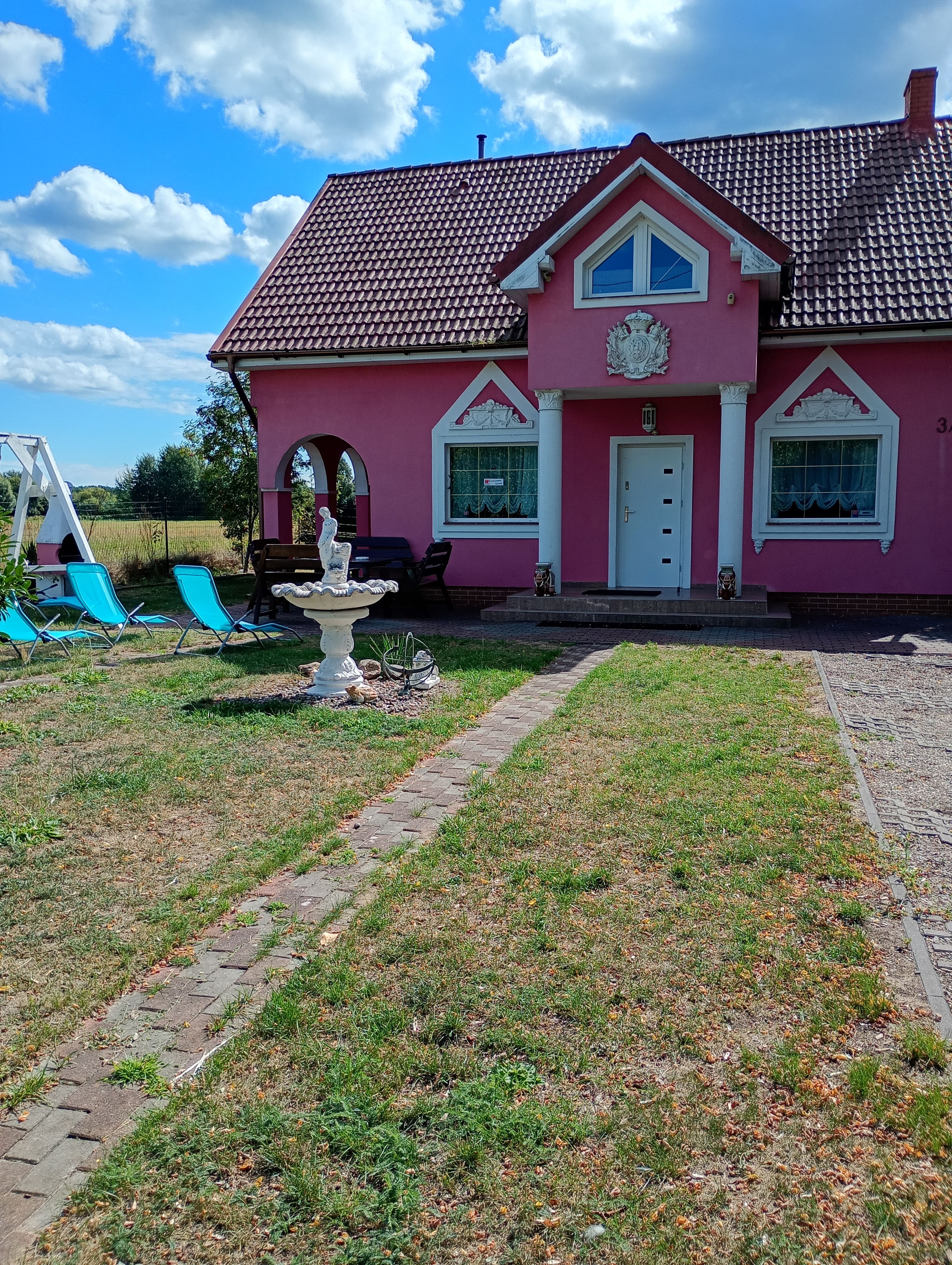 A pink house with a tiled roof, a front porch, and a small garden area with a fountain.