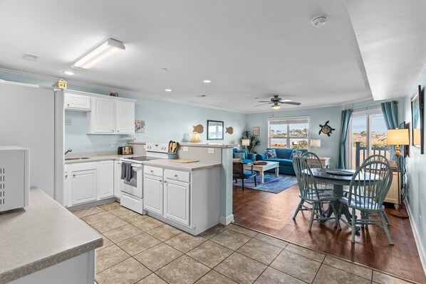 A modern kitchen with white cabinets, a dining area with a table and chairs, and a view of the outdoors through large windows.