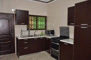A kitchen with dark wooden cabinets, a stainless steel sink, a microwave, and a gas stove. - FA Homes (Oyarifa)