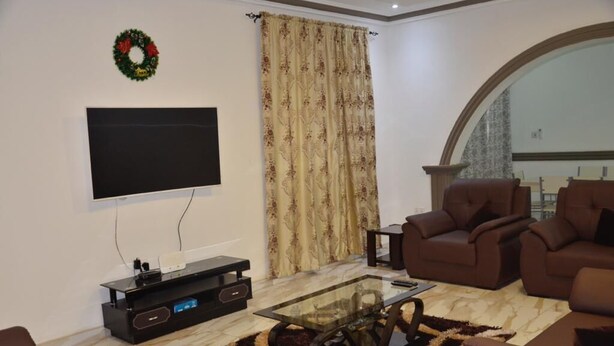 Een woonkamer met een flatscreen televisie, een zwarte tv-kast, twee bruine banken, een glazen salontafel en een gordijn met een patroon.