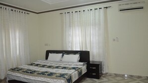 Een slaapkamer met een bed, gordijnen, een airconditioning en een betegelde vloer.