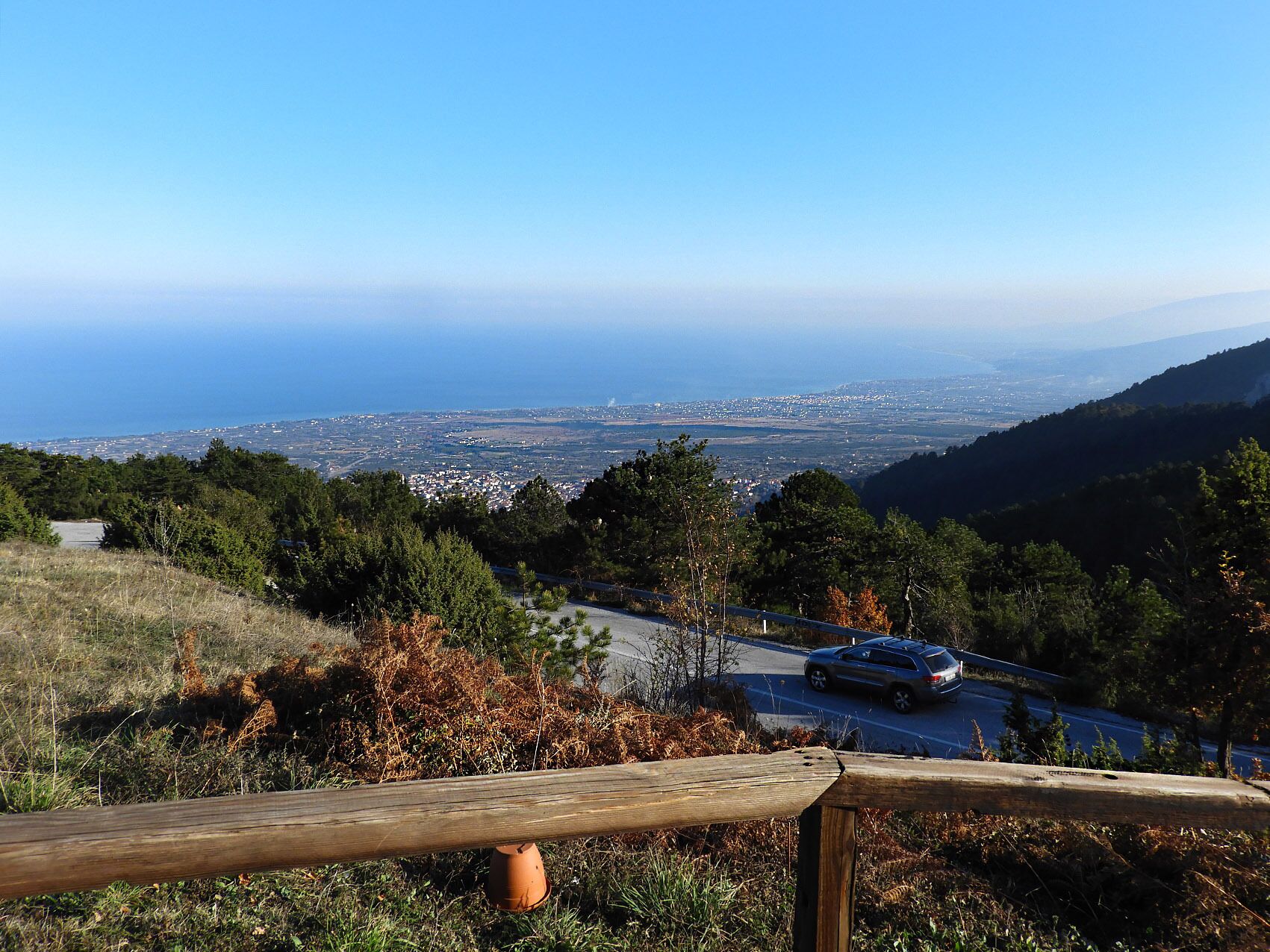Uma vista panorâmica com estrada, árvores e um horizonte urbano ao longe.
