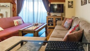 A living room with a sofa, a table with a laptop, a TV, and a cabinet. - Seaview family apartment at Olympus - PanoramaLoft (Litochoro)