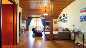 A spacious living area with wooden flooring, a sofa, a coffee table, and a TV stand. - Seaview family apartment at Olympus - PanoramaLoft (Litochoro)