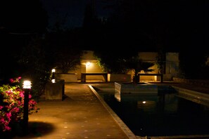 A nighttime pool area with a paved walkway, a pool, and some greenery.