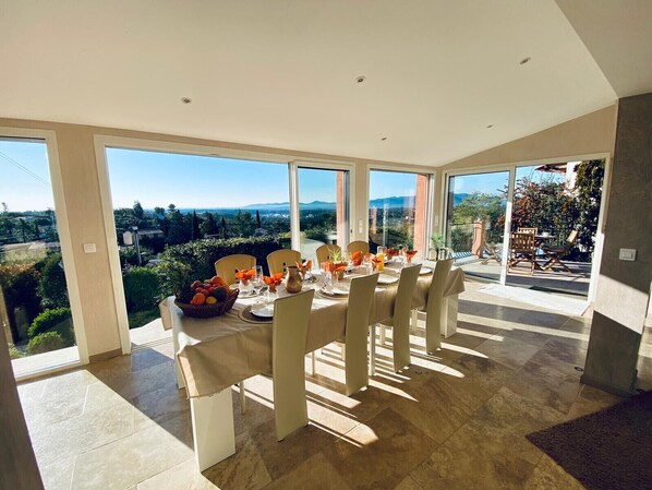 A dining area with a table set for six, large windows, and a view of the landscape.