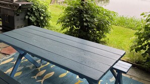 Un espace extérieur abrité, équipé d’une table de pique-nique, d’un barbecue et offrant une vue sur un lac.