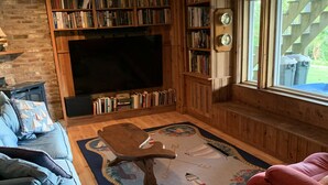 Un salon chaleureux avec une cheminée, une grande bibliothèque, un téléviseur à écran plat et un coin salon confortable composé de deux canapés et d’un tapis à motifs.
