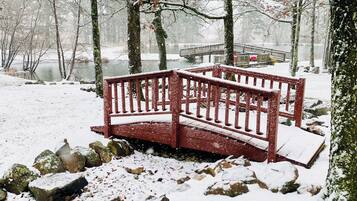 A snow-covered bench in a park with a bridge in the background.