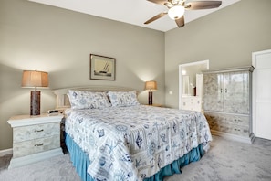A bedroom with a bed, two bedside tables with lamps, a dresser, a ceiling fan, and a framed picture on the wall.