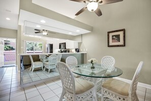 A modern kitchen with white cabinets, a glass dining table, and wicker chairs.