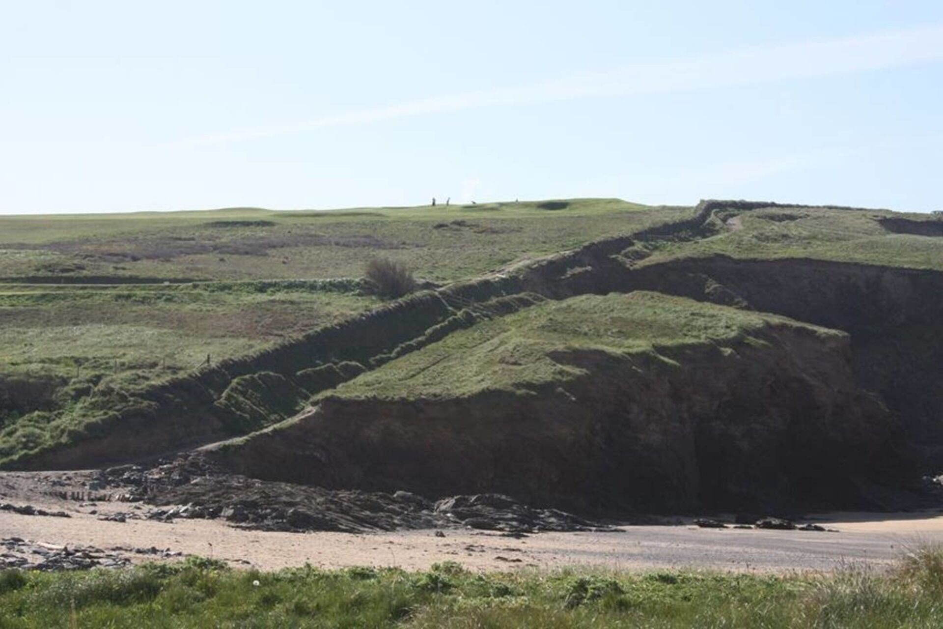 A coastal landscape with grassy hills and a sandy beach.