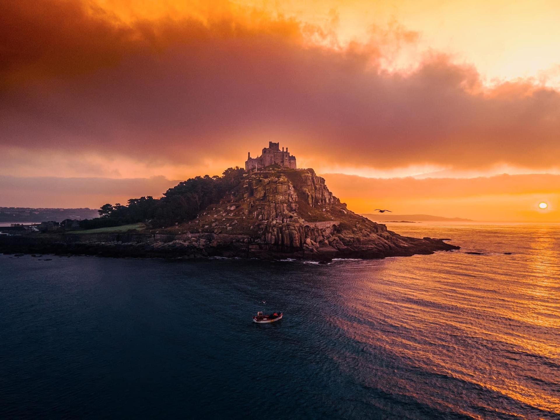 A castle on a rocky island with a boat in the water.