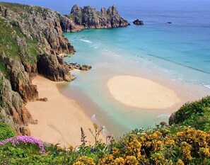 Paisagem costeira com uma praia arenosa, falésias rochosas e águas azul-claras.