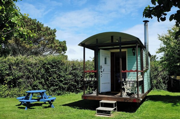 A small, single-room cabin with a porch, a picnic table, and a chimney.