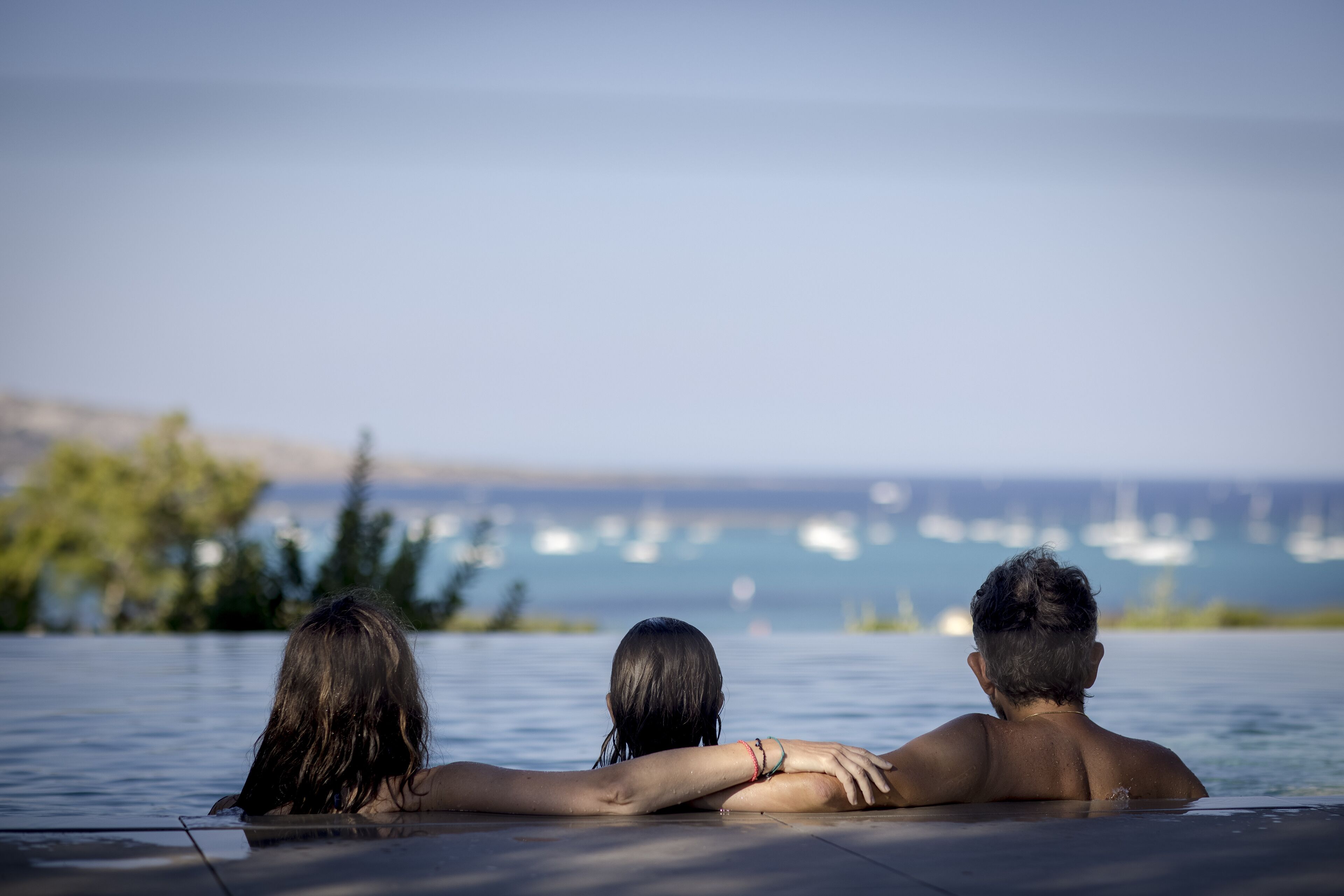 Drei Personen entspannen sich in einem Pool mit Blick auf das Meer und Boote.