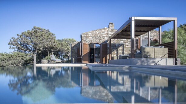 Uma casa moderna com fachada de pedra, piscina e mobiliário de exterior.