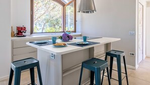 Cozinha moderna com ilha central, banquetas, máquina de café e janela com vista para árvores.
