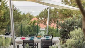 Uma área de refeições ao ar livre com uma mesa posta para dois, rodeada por vegetação e vista para um horizonte urbano distante.