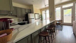 Eine Küche mit einer langen Kochinsel, Barhocker, einem Kühlschrank und einer Kaffeemaschine.
