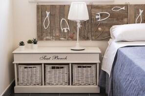 Ein Schlafzimmer mit einem Bett, einem Nachttisch mit Lampe, einer Sitzbank mit dem Aufdruck 'Seat Bench' und Wanddekoration.