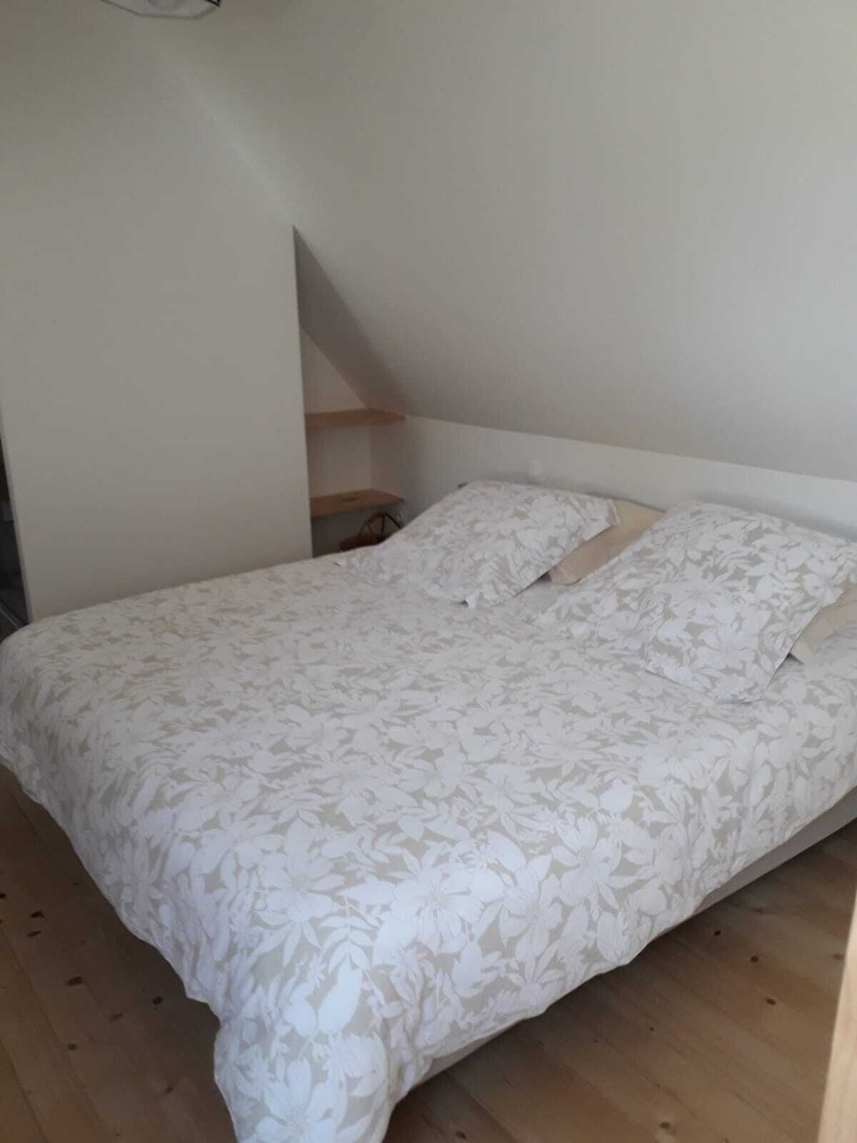 Una camera da letto con un letto, pavimento in legno e soffitto spiovente.
