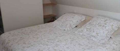 Una camera da letto con un letto, pavimento in legno e soffitto spiovente.
