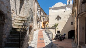 Une ruelle étroite pavée, bordée de bâtiments historiques en pierre, avec un escalier menant à un balcon situé au deuxième étage.