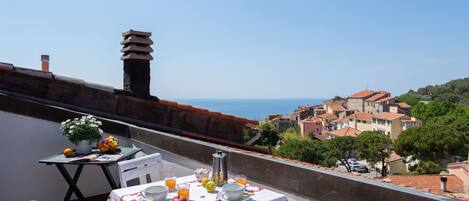 A balcony with a table set for breakfast, overlooking a coastal town.