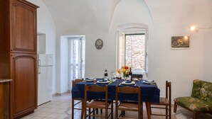 Un coin repas avec une table dressée pour quatre personnes, un buffet en bois, une fenêtre donnant sur un beau paysage et une chaise agrémentée d’un coussin à motifs floraux.
