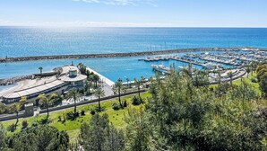 Un port de plaisance avec des bateaux amarrés, un grand bâtiment doté d’un toit incurvé et une digue rocheuse.
