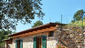 Un edificio de piedra con contraventanas verdes, techo de tejas y un muro de piedra.