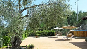 Un patio al aire libre con un muro de piedra, dos sillones, una mesa y un gran paraguas.